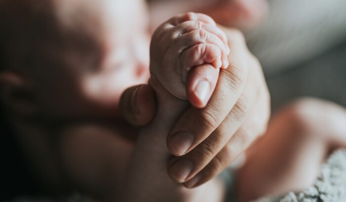 Baby and mother holding hands, for article on cesarean birth survival