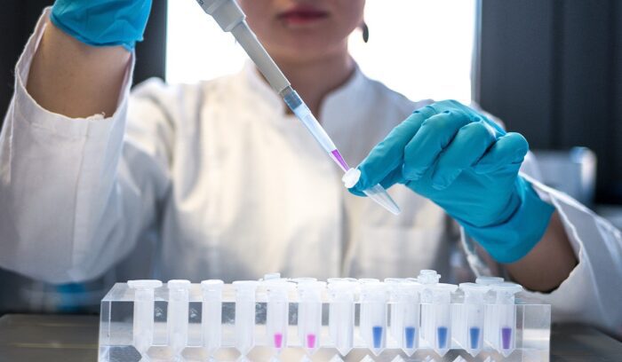 Female scientist pipetting colored chemicals into a tube, for article on CAR T-cell therapy