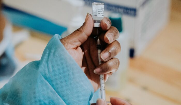 Hand holding a vial and syringe, for article on malaria vaccine rollout
