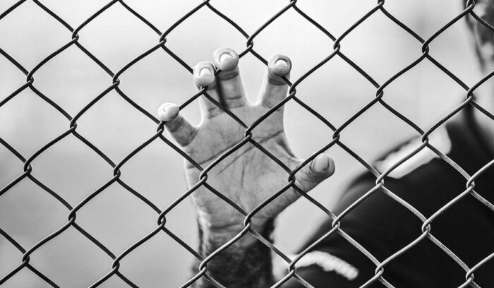 Hand holding on to chain link fence, for article on Norwegian prison reform
