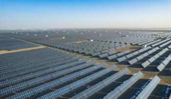 A vast solar farm at sunset with wind turbines on the horizon for an article about 100% renewable energy