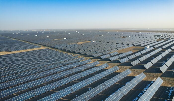 A vast solar farm at sunset with wind turbines on the horizon for an article about 100% renewable energy