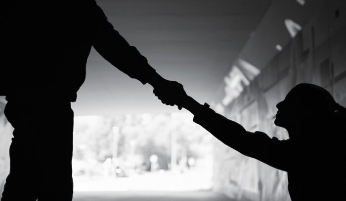 Man giving a helping hand to woman in need sitting on dark street