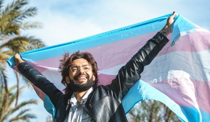 Person happily holding a trans pride flag, for article on gender-affirming care