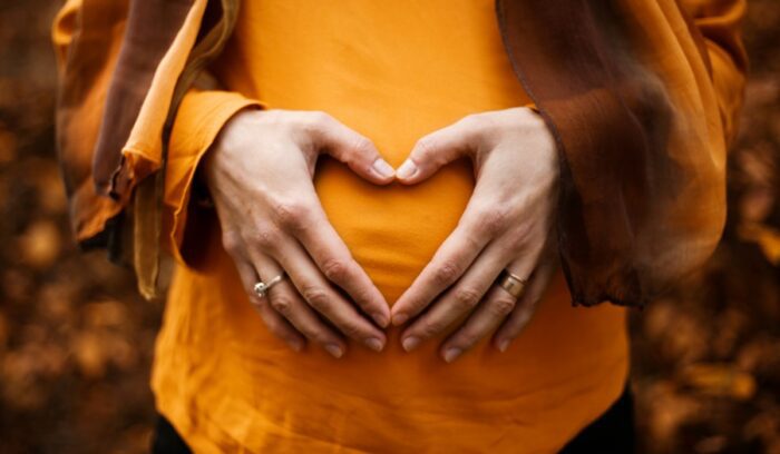 Person touching pregnant belly with hands forming a heart, for article on LGBTQ+ fertility coverage