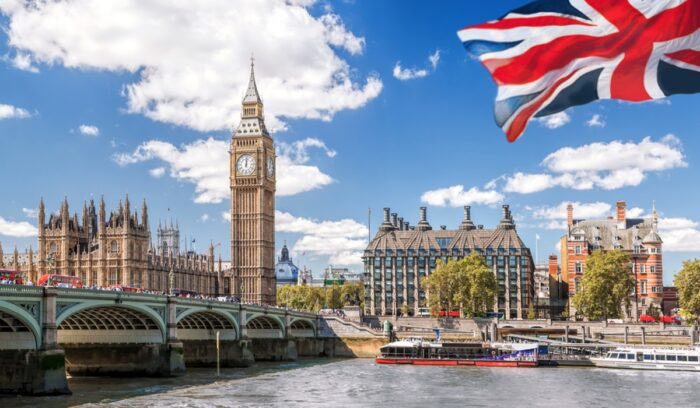 Big Ben with bridge over Thames and flag of England against blue sky in London