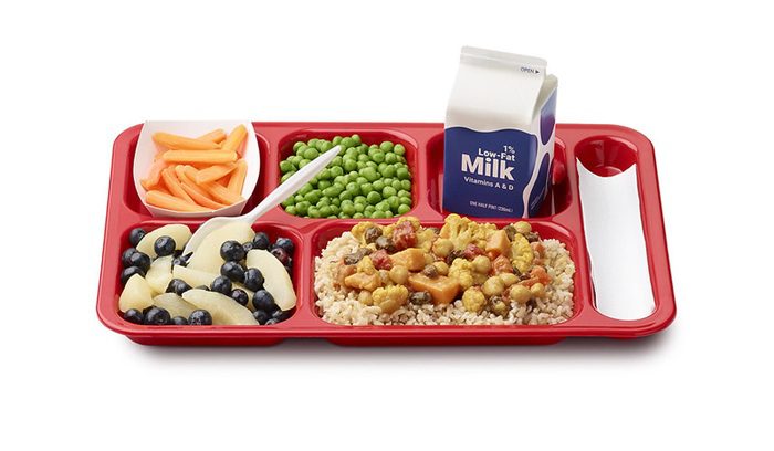 A school cafeteria serving hot lunch to children for an article about free school meals expansion — 12 words