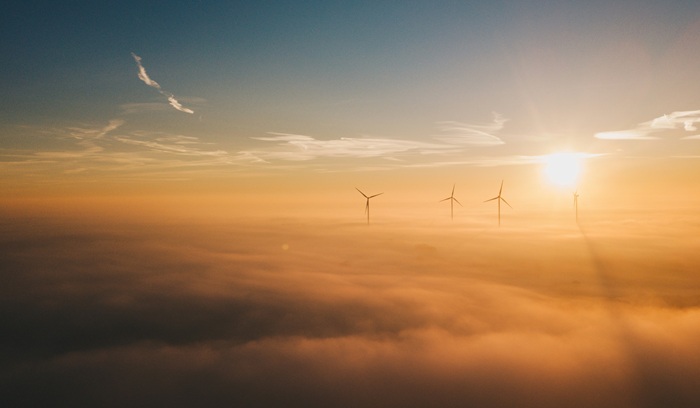 Sun shining with wind turbines rising above clouds