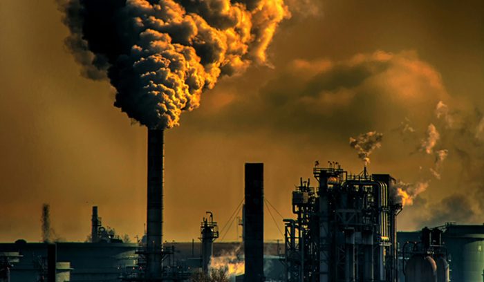 Oil refinery towers silhouetted against a hazy sky for an article about the TotalEnergies greenwashing ruling
