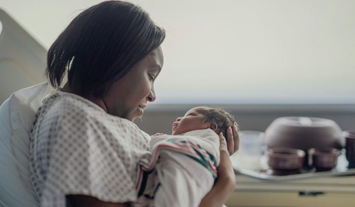 A mother holding a newborn in a hospital setting for an article about the Detroit RxKids cash program