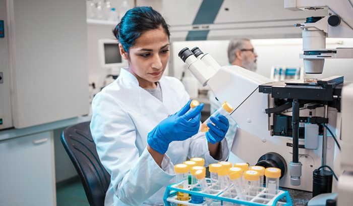 A researcher examining cancer cell slides under a microscope for an article about UK cancer death rates