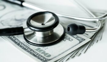 Stethoscope on top of a stock of hundred dollar bills, for article on medical debt cancellation, for article on medical debt cancellation, for article on medical debt cancellation
